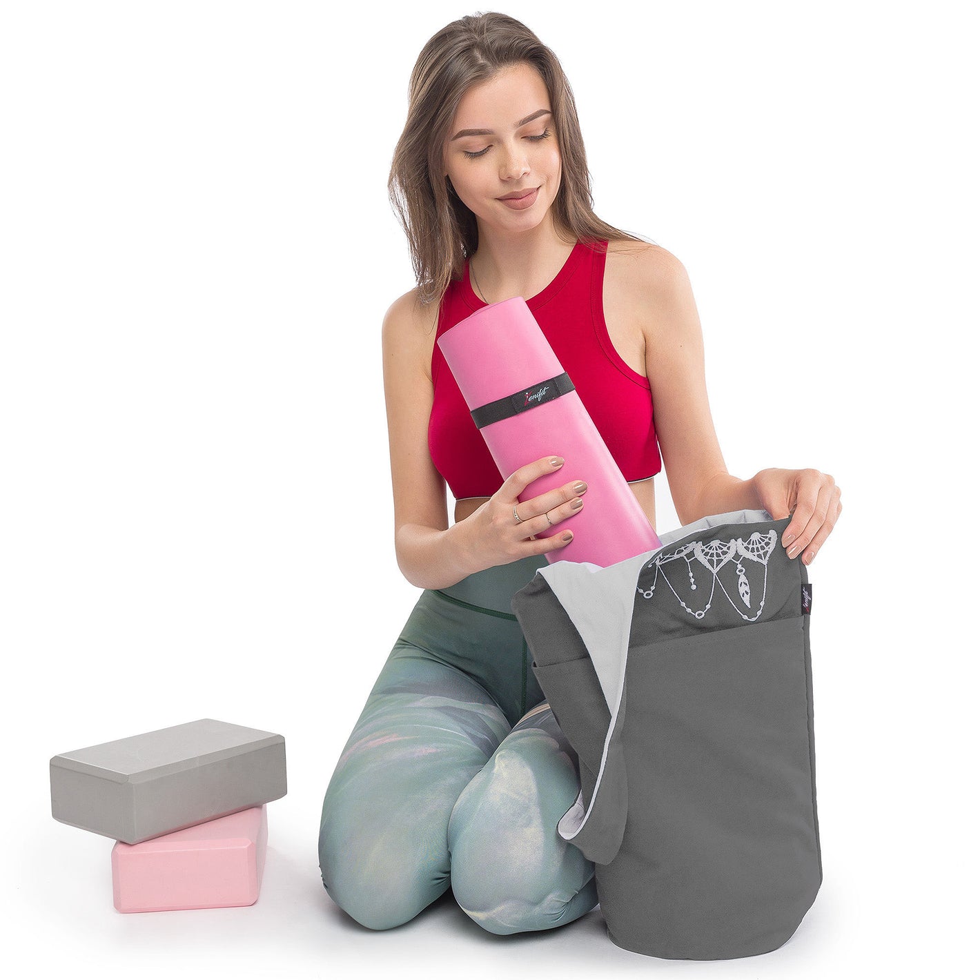women putting yoga mat in th yoga bag on her knees with yoga blocks next to her